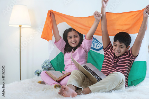 Fotografía Indian brothers and sisters with laptops on lap sitting on bed, holding Indian f