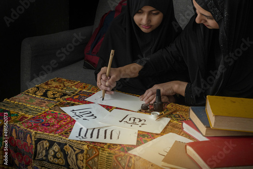 Little Muslim girl and Mom wearing hijab or nigab, holding her and write Arabic alphabet, Arabic letters mean the name of Muslim god "Allah"