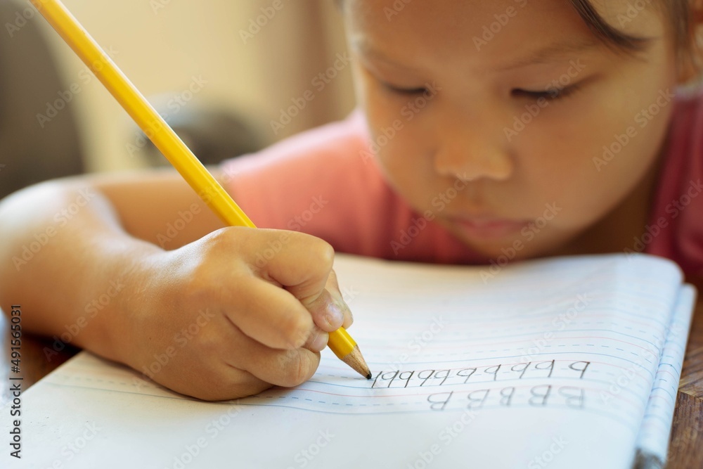A kindergarten student holding a pencil, learning how to write the alphabets. children education A kindergarten student holding a pencil, learning how to write the alphabets. children education