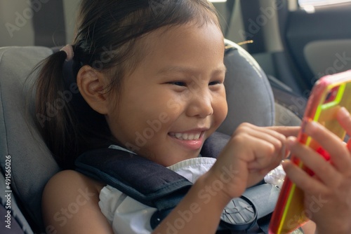 A little kid holding a phone while in the car seat, watching educational videos and games.