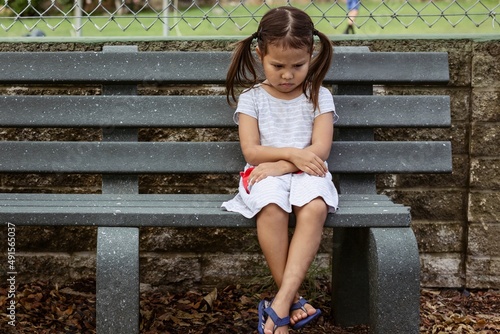 Unhappy little girl sitting alone outside at school.