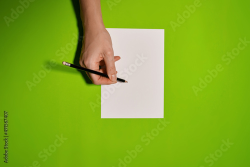 Overhead shot of female hands writing with pen over empty white sheet of paper on green background