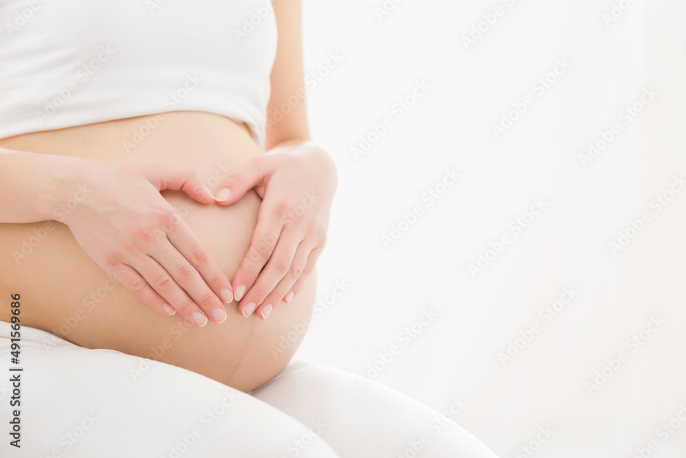 Heart shape created from young adult pregnant woman hands on big naked belly isolated on white background. Pregnancy time. Baby expectation. Love, happiness and safety concept. Empty place for text. Heart shape created from young adult pregnant woman hands on big naked belly isolated on white background. Pregnancy time. Baby expectation. Love, happiness and safety concept. Empty place for text.