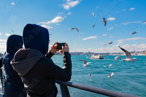 Teens taking photograph of seagulls with mobile phones. Back view. Unrecognizable people.