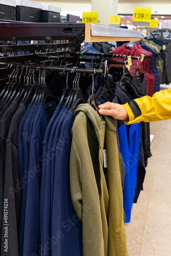 Man hand touches some shirt from a lot of clothes and choose some ıtem in clothing store. Unrecognizable person.