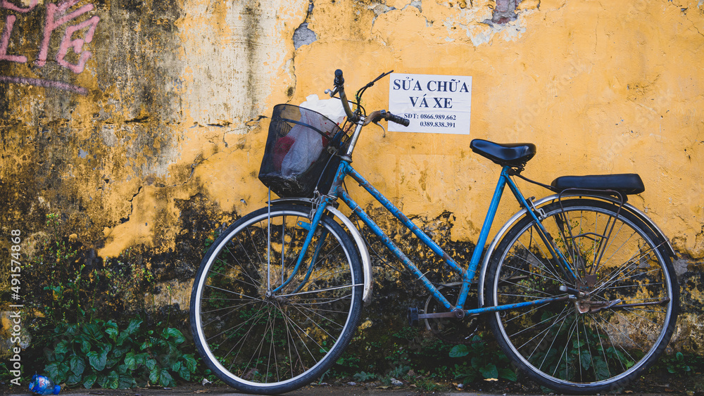 old Blue bicycle in front of yellow wall