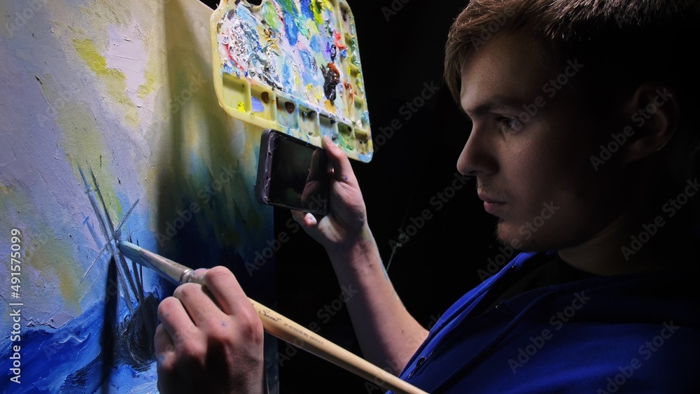 Fototapeta premium Artist copyist paint seascape with ship in ocean. Craftsman decorator draw as boat sail on blue sea with acrylic oil color. Draw finger, brush, knife palette. In hand of cellphone tablet computer pc.