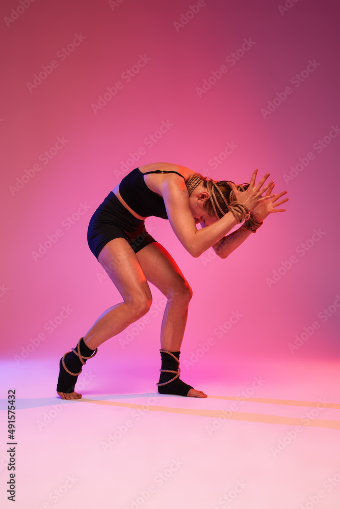 Fototapeta premium Portrait of female anger, animal instinct, demonstrating incredible flexibility with the movement of animal flow in the studio on a on pink blue gradient background.