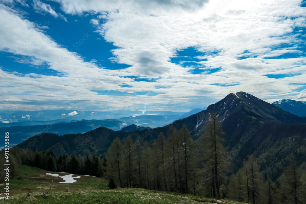 Scenic view on Hahnkogel (Klek) through a dense forest in the Karawanks in Carinthia, Austria. Borders between Austria, Slovenia, Italy. Triglav National Park. Snow capped hills. Woodland, Wanderlust