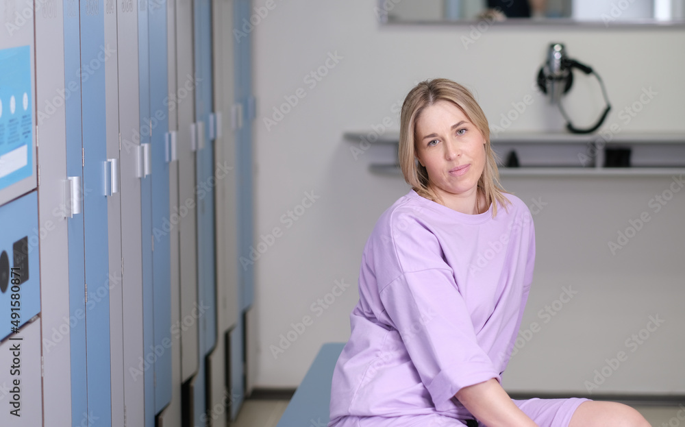 woman getting rest in change room of fitness club after workout. locker room in health center. woman sitting on a bench in front of lockers. woman getting rest in change room of fitness club after workout. locker room in health center. woman sitting on a bench in front of lockers.