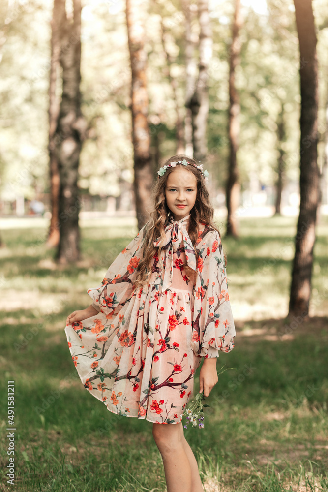 Smiling blonde teen girl posing in summer garden. Wearing flower wreath outdoors. Smiling blonde teen girl posing in summer garden. Wearing flower wreath outdoors.