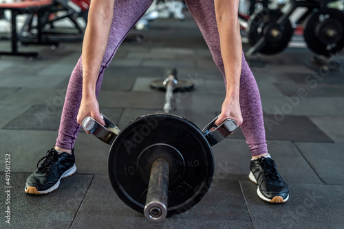 Athletic young woman doing exercise lifting barbells at gym