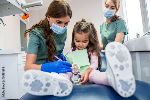 Female stomatologist showing little girl how correctly brushing teeth