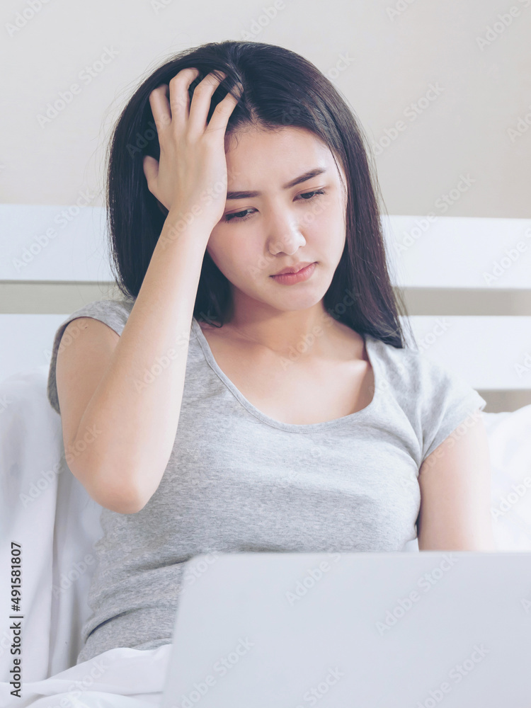 Young beautiful woman sitting on bed, She use laptop feel serious and headache Young beautiful woman sitting on bed, She use laptop feel serious and headache