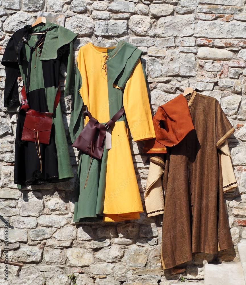 Colorful medieval dresses,used for reenactments or costumes, hanging on an old stone wall.
