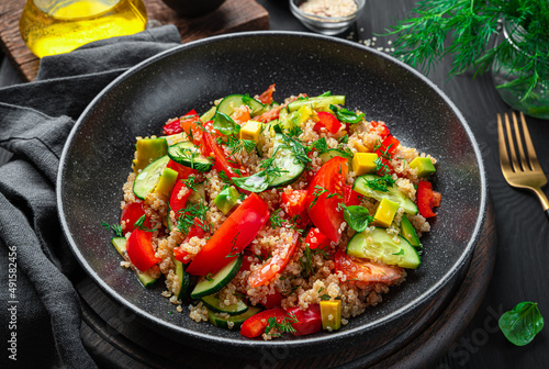 Salad with quinoa, avocado, tomato and cucumber on a dark background