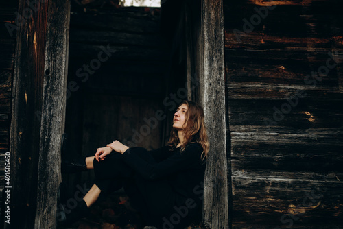 beautiful Ukrainian girl in black clothes near the old wooden house. The war in Ukraine. Portrait of a woman on a dark wooden background. Old abandoned wooden house. Old wooden window frame © Anhelina Tyshkovets
