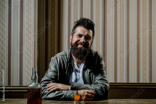 Cheerful bearded sman is drinking expensive whisky. Stylish elegant bearded man holds whiskey glass in pub. photo