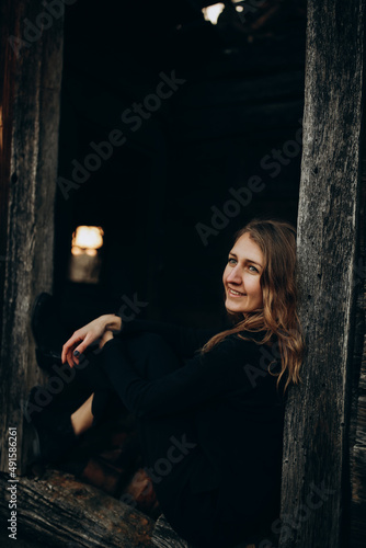 beautiful Ukrainian girl in black clothes near the old wooden house. The war in Ukraine. Portrait of a woman on a dark wooden background. Old abandoned wooden house. Old wooden window frame