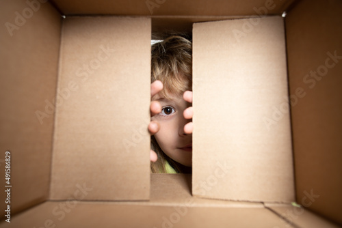 Happy child with cardboard box, unpacking parcel from internet store. Kids client satisfied with fast delivery service. Child with open box. Close up eyes looking.