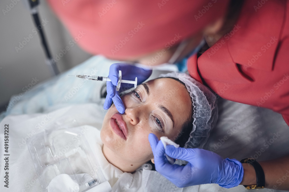 Cosmetologist doing painful lip augmentation procedure with hyaluronic acid. The beautician