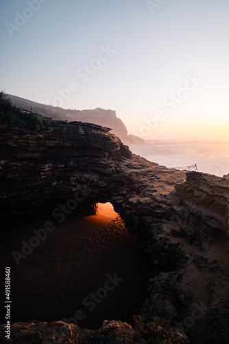 Last sunbeam entering through a hole in a cliff with the sunset in the background.