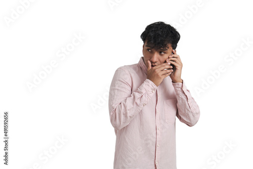 Young peruvian man whispering on the phone. Isolated over white background.