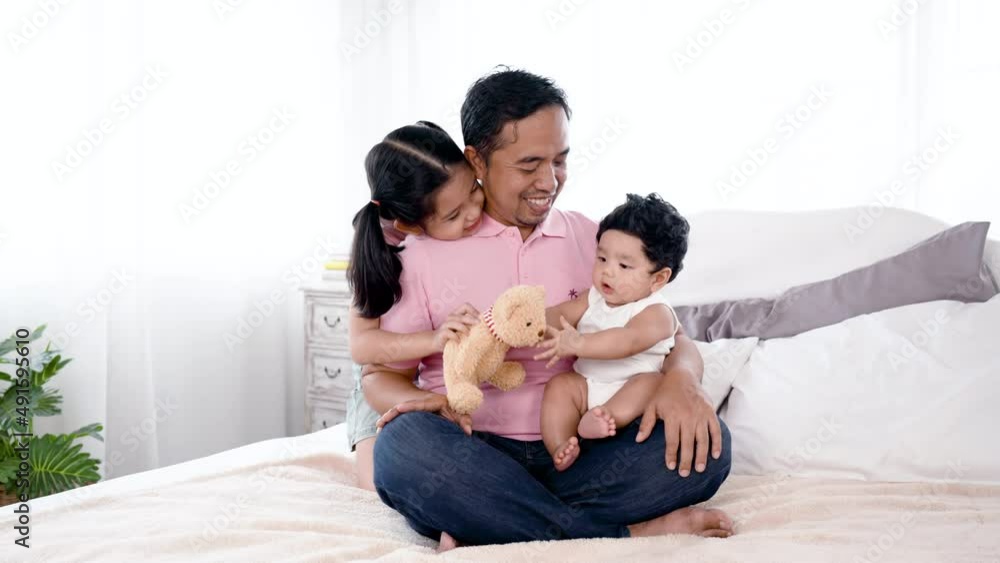 4K 50fps, Asian father holding an adorable newborn boy playing brown teddy bear on the bed, and an older sister hugging dad behind him playing with his younger brother, happy face.Family and Healthy. 4K 50fps, Asian father holding an adorable newborn boy playing brown teddy bear on the bed, and an older sister hugging dad behind him playing with his younger brother, happy face.Family and Healthy.