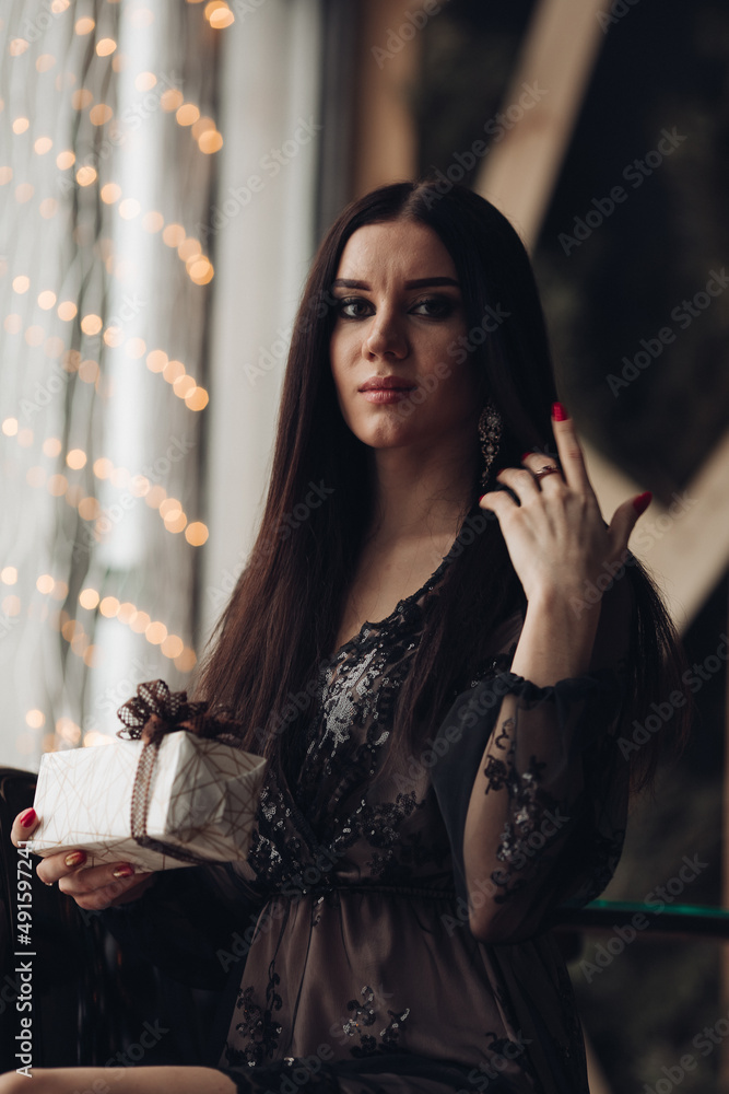 Gorgeous brunette model in black dress and heels in armchair.