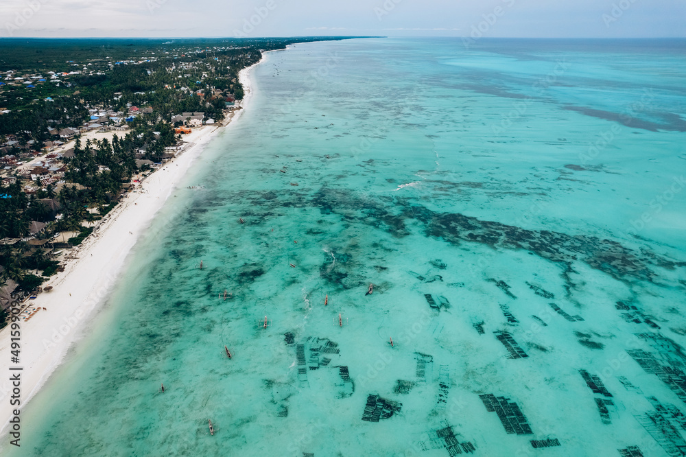 Aerial view of the fishing boats on tropical sea coast with sandy beach. Summer holiday on Indian Ocean, Zanzibar, Africa. Landscape with boat, buildings, transparent blue water. Top view