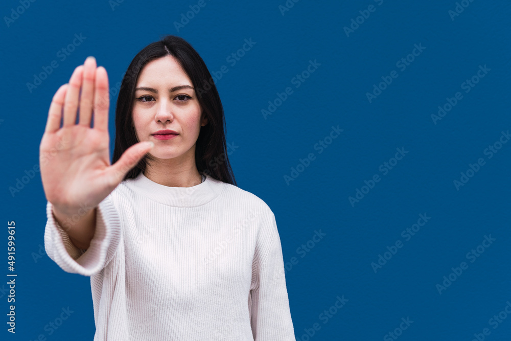 Fototapeta premium Displeased asian woman standing with hand on hip and pointing with finger while showing stop sign