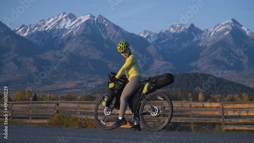 The woman travel on mixed terrain cycle touring with bikepacking. The traveler journey with bicycle bags. Sport tourism bikepacking, bike, sportswear in green black colors. Mountain snow capped.