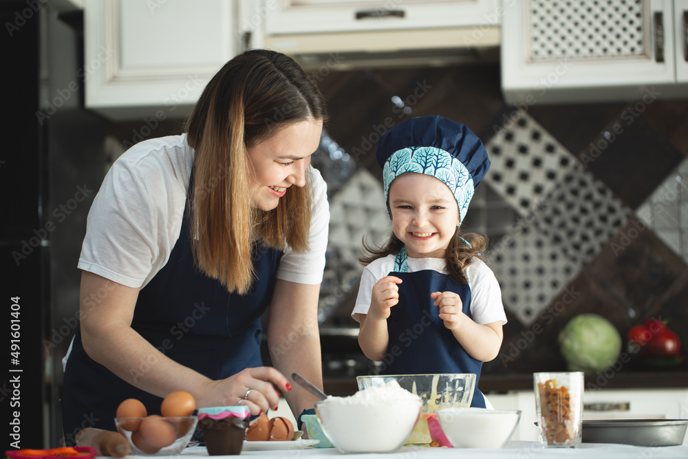 Young mother and daughter in the kitchen preparing cupcakes and smiling, laughing. Young mother and daughter in the kitchen preparing cupcakes and smiling, laughing.