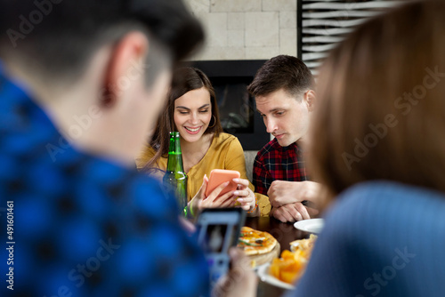 Group of friends in a cafe with pizza and beer having fun. The girl shows the guy a funny photo on the phone