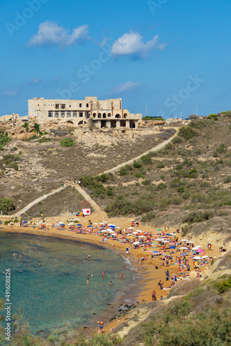 Sunbathers on the beach at Għajn Tuffieħa Bay, Malta, with a derelict hotel overlooking them. photo