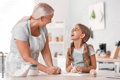 Mature woman with her little granddaughter making dough in kitchen