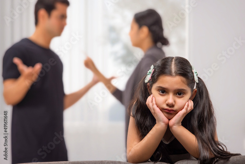 Portrait of a sad girl child with hands on cheek and parent arguing behind photo