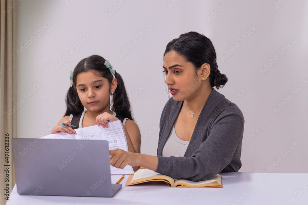 Girl submitting homework through online class using laptop and mother sitting beside