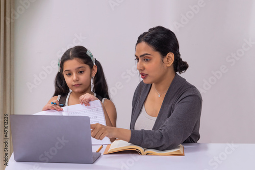 Girl submitting homework through online class using laptop and mother sitting beside photo