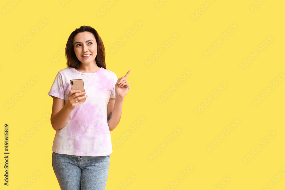 Woman with mobile phone pointing at something on yellow background. E-mail concept Woman with mobile phone pointing at something on yellow background. E-mail concept