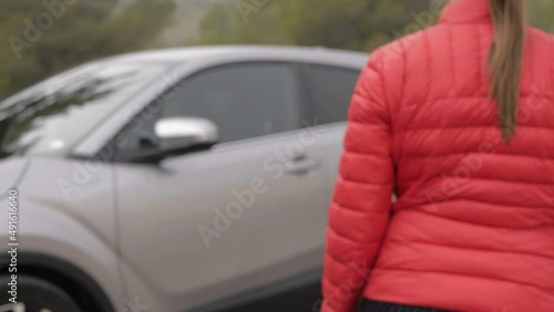 Close-up the female hands opening the car with a key fob. Woman in red jacket gets into the grey SUV auto.