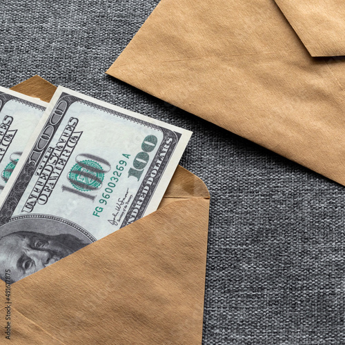 Concept on the topic of collecting money to pay taxes and debts. A square photo of American hundred-dollar bills in a craft paper envelope.