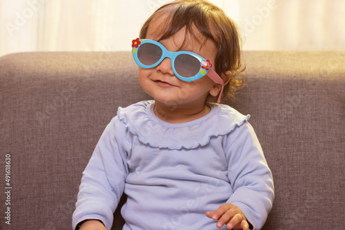 Portrait of a cute baby wearing sunglass while sitting on sofa in living room photo