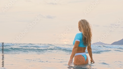 SLOW MOTION GLOW MIST GOLD SUNSET CINEMATIC VIEW: Attractive woman standing on water sea. Girl stand in turquoise swimsuit. Freedom paradise holiday vacation summer beach, seaside landscape concept