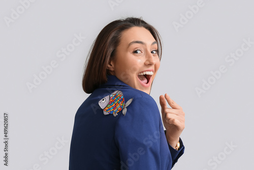 Sticker Young woman with paper fish attached to her back on grey background