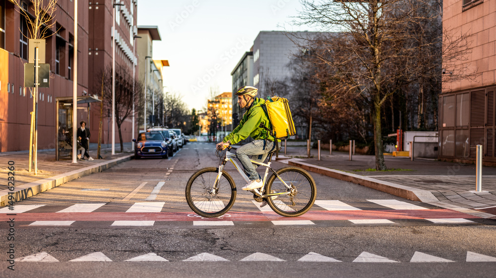 Fast and ecologic delivery service, deliveryman at work, riding city street to handing over takeaway food, boxes and dociments, black, white and yellow bycicle, yellow backpack, green jacket