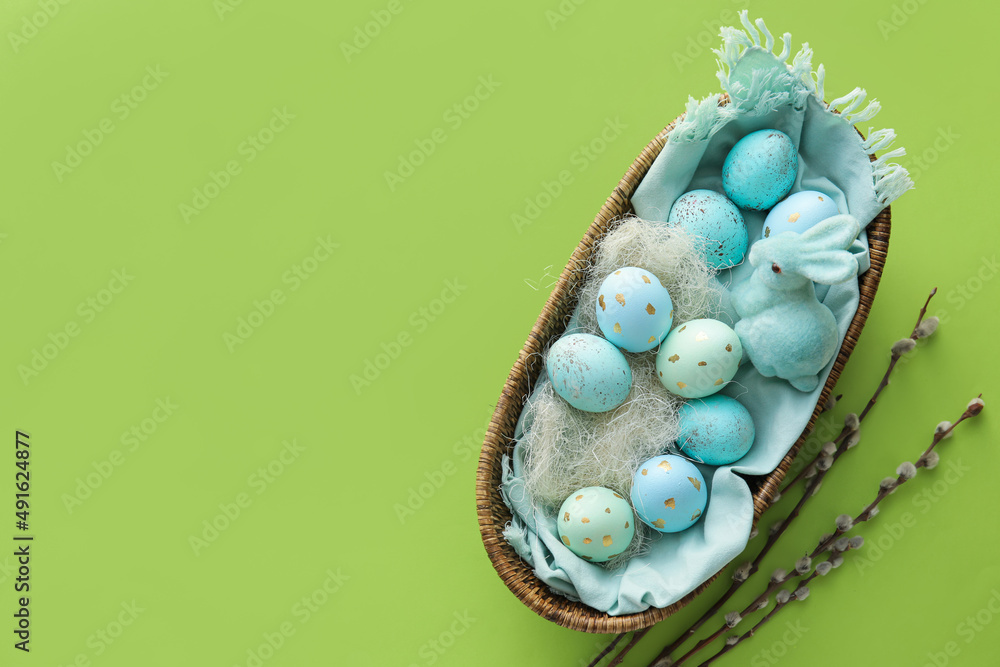 Basket with painted Easter eggs and willow branches on green background
