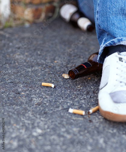 Youth gone bad. Closeup shot of a person sitting next to discarded cigarette butts and beer bottles.
