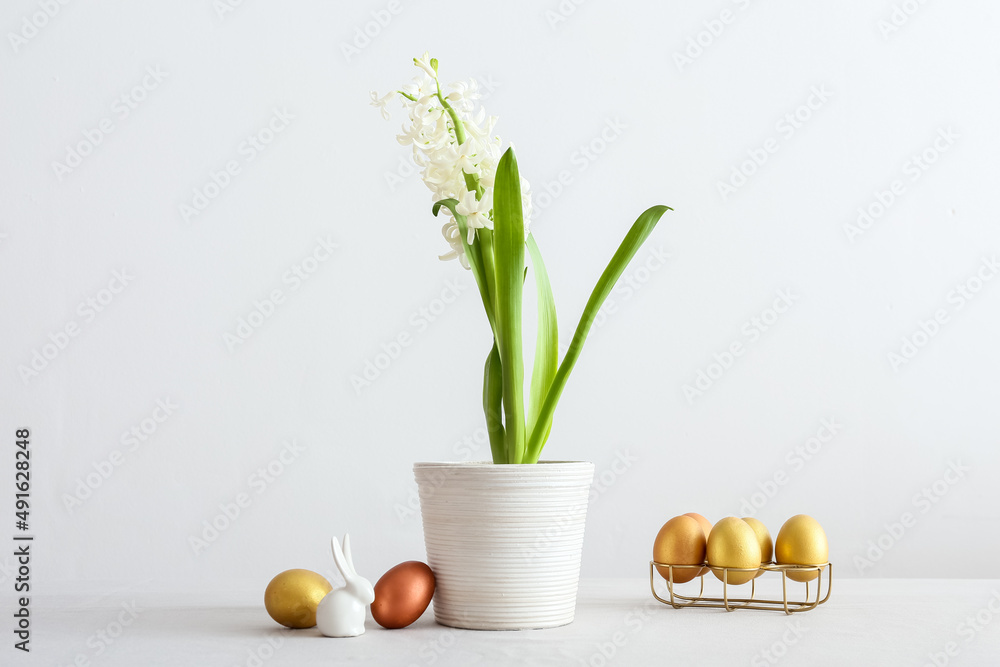 Fototapeta premium Pot with beautiful hyacinth plant, Easter bunny and eggs on light background