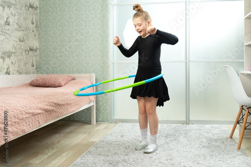 A child spins a hoop at home in the living room. Little girl with a dancing black dress twists a hoop at home in the living room